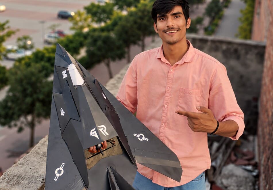 Vinay holding the F-117 Nighthawk model aircraft he built, on a rooftop at sunset