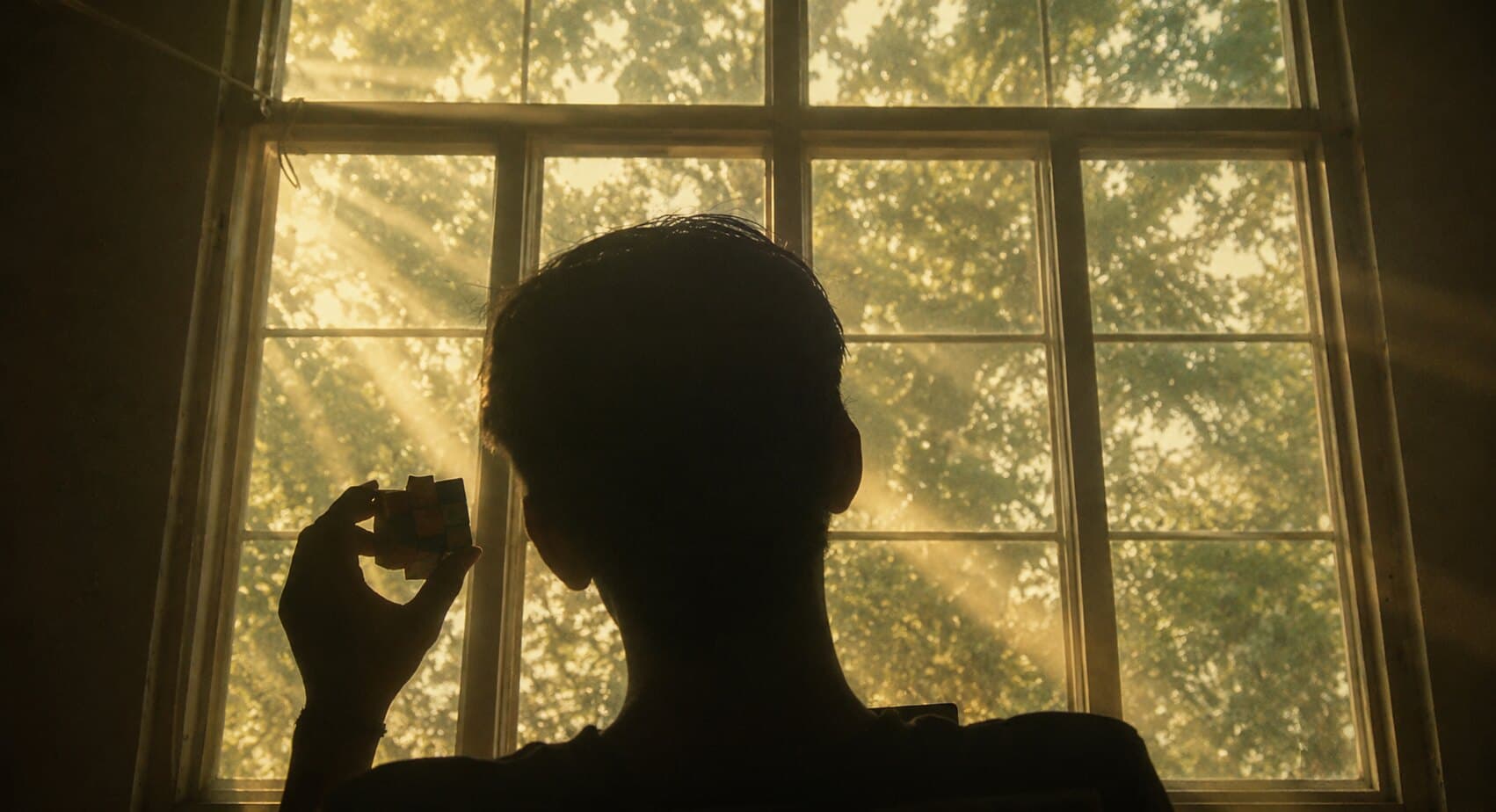 Vinay Tiwari silhouetted against a sunlit window, holding a Rubik's cube